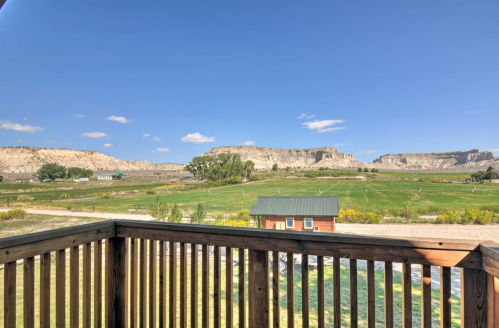 View from a wooden balcony overlooking green fields and rocky cliffs under a clear blue sky.